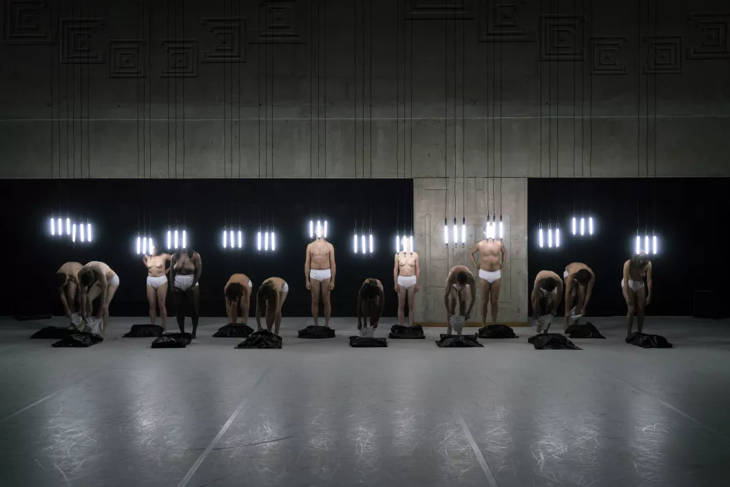 a photo of dancers at the back of the stage wearing white shorts, with tubes of light suspended above their heads