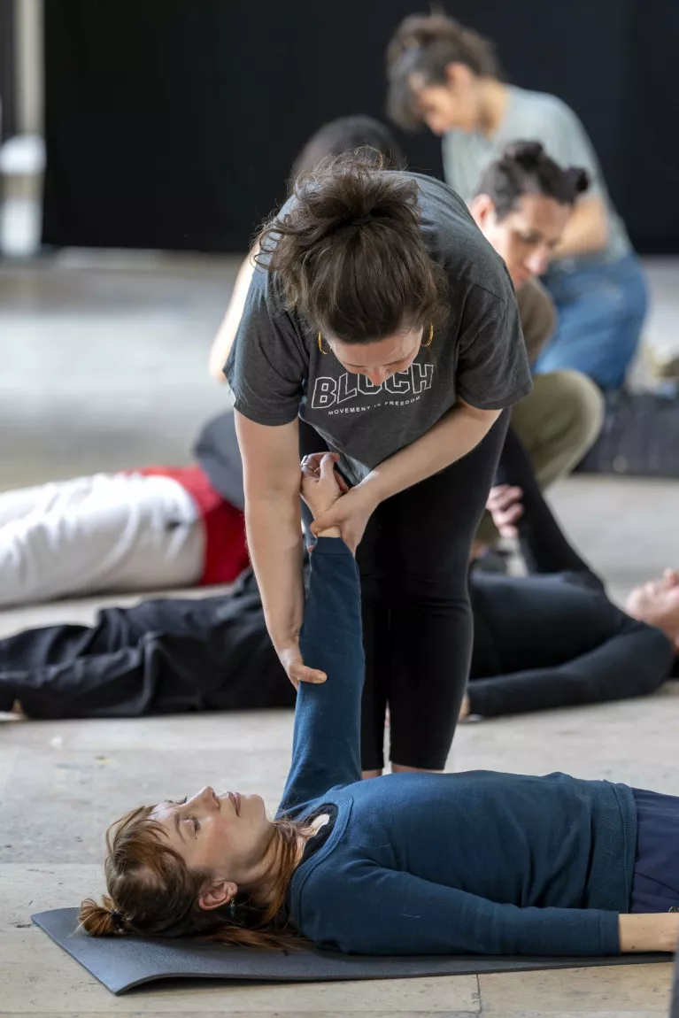 Une personne lève le bras d'une autre personne qui est allongée sur le dos. La scène se situe lors d'un cours de kinésithérapie.