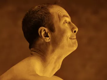 A man is shown in profile, his head raised toward the sky, bathed in golden light. His facial features are tense.