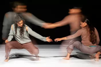 A photo from Marah Haj Hussein & Nur Garabli show "In relation to whom? مرتاحة؟" showing two dancers squatting down and trying to hold hands. The photo is blurry.