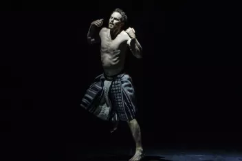 Photo from Boris Charmatz's play “SOMNOLE,” featuring a shirtless man dancing in the dim light