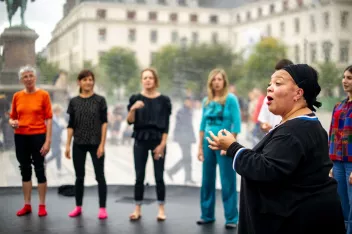 Photographie de Dalila Khatir en train de faire chanter un groupe de personne en cercle dans le second plan de l'image