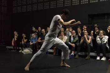 photo du spectacle "À bras-le-corps" avec un danseur vêtu de blanc et des spectateurs au second plan