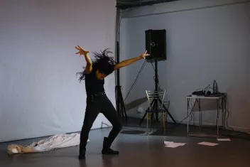 a photo of a performance featuring Betty Tchomanga dressed in black, with her arms raised