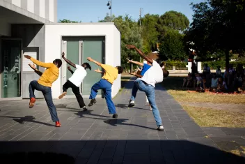 photo of four dancers outdoors, seen from behind as they perform the same movement