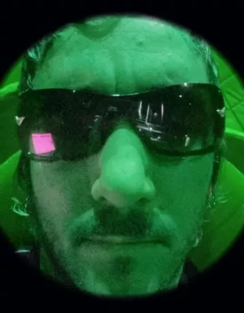 close-up of Tom Grand Mourcel wearing sunglasses, illuminated by a green light