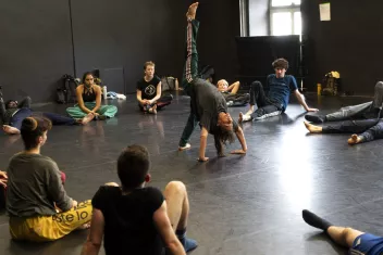 Dancers sitting in a circle watching a dancer perform a backbend
