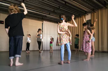 Photo of children standing in a circle and raising their hands during a dance workshop