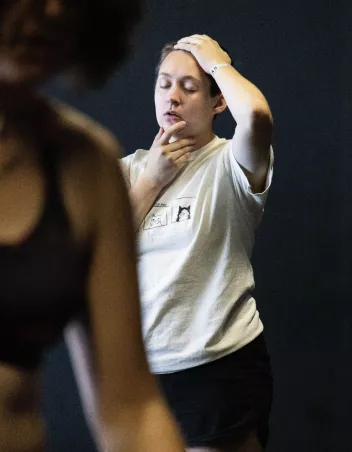 A photo of a dancer standing with her eyes closed, one hand on her throat and the other on her head