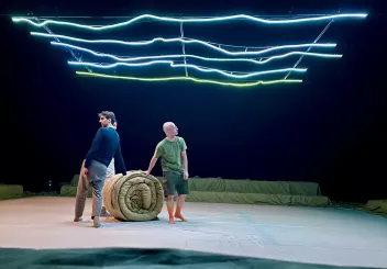 3 danseurs autour d'un matelas beige enroulé. 