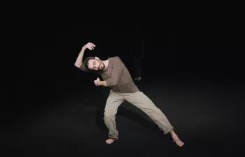 Danseur penché sur la droite vêtu d'un pantalon beige et d'un t-shirt marron