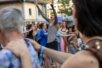 A photo taken in the courtyard of the SUBS in Lyon showing participants standing in a circle, with their arms around each other’s shoulders, surrounding a choreographer holding a microphone