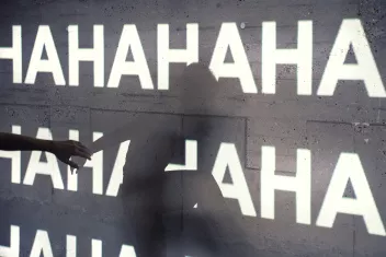 The shadow of a dancer in front of a wall onto which the letters A and H are projected