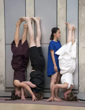 Three dancers are doing handstands; one of them is standing