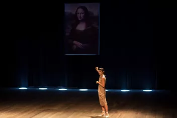Photo du spectacle "Domínio Público" avec une interprète qui montre le tableau de La Joconde