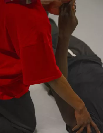 A person is moving the arm of another person who is lying on the floor