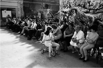 Photo noir et blanc en extérieur d'une danseuse sur un trycicle devant un public assis 