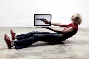 Photo of a dancer lying on the floor holding a laptop displaying an image of a gun