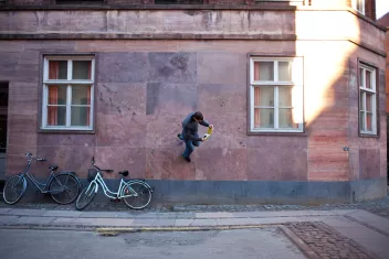 Photo of a man reading whilst walking along a wall