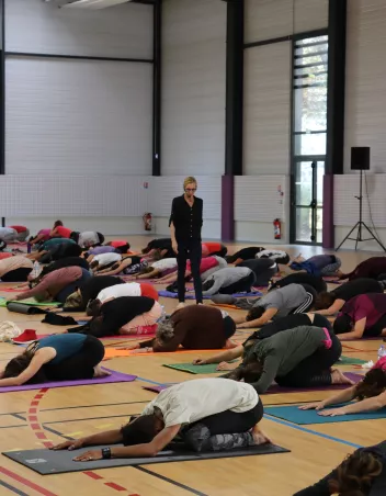 photo d'un atelier de yoga avec des participants en pose de l'enfant sur des tapis et Mathilde Monnier debout