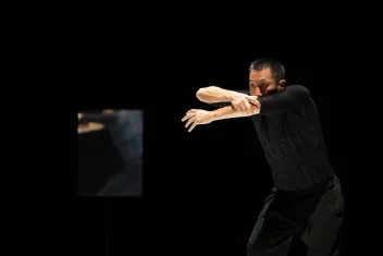 A dancer dressed in black is holding his forearms