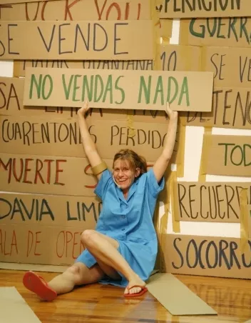 photo of a performance featuring a female performer sitting on the floor and holding a sign that reads "No vendas nada"