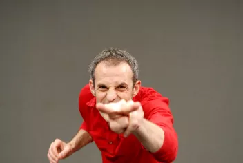 Photo de Xavier Le Roy avec une chemise rouge, qui pointe deux doigts face à l'objectif