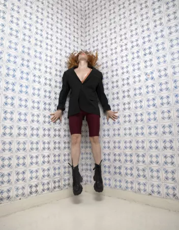 A photo of a dancer leaping, head held high, in the corner of a tiled room