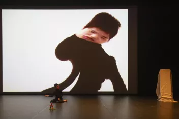 The artist No Anger on stage, sitting on the floor in front of a giant screen that distorts his image