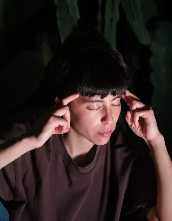 A photo of Marcela Santander Corvalán with her eyes closed, a finger on each temple. 