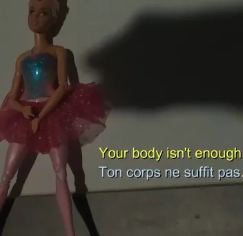 Photo d'une barbie avec l'ombre d'une main et l'inscription "Your body isn't enough, ton corps ne suffit pas"