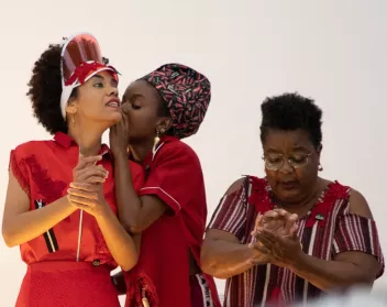 3 femmes habillées en rouge. Pendant qu'une d'entre elle malaxe une pâte, les deux autres se chuchotent des choses à l'oreille