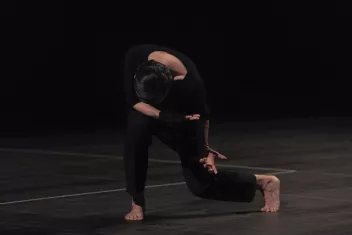Photo of a dancer bent towards the floor, dressed in black