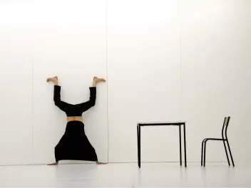 photo d'un spectacle avec un danseur en équilibre contre un mur blanc, une table et une chaise noires