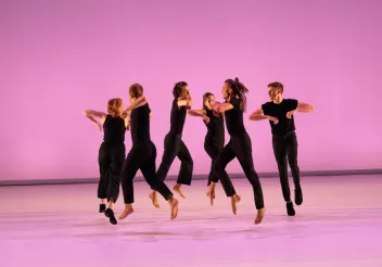 Danseurs sur décor rose habillés en noir en train de sauter