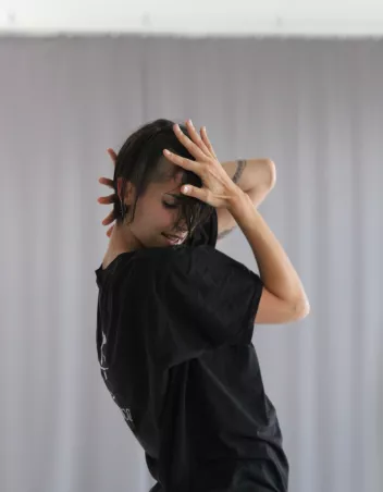 photo de Sofia Nappi en représentation ; vêtue d'un t-shirt noir, une main sur le visage, l'autre derrière la tête