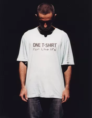 A dancer stands looking at his white T-shirt, which reads ‘one T-shirt for life’