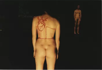 a photo of a naked body seen from behind, with a heart drawn in red felt-tip pen, facing a naked male body