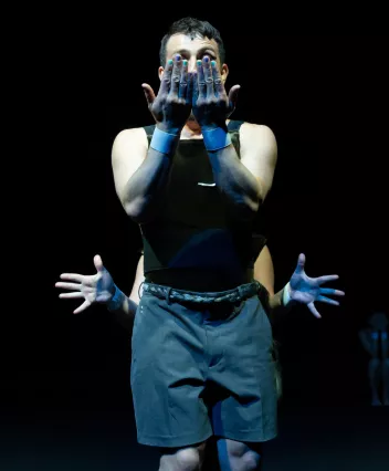 Un danseur a ses mains devant le visage, unOne dancer has his hands in front of his face; a second dancer is hiding behind him, with only his hands protruding from either side of the first dancer’s bodysecond se cache derrière lui et ne fait dépasser que ses mains de chaque côté du corps du premier danseur