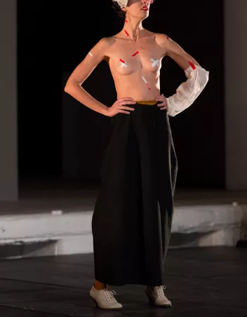 a photo of a dancer, bare-chested and wearing black trousers, covered in bits of white and red sticky tape