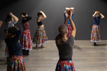 Danseurs et danseuses les bras au dessus de la tête, vêtus d'un t-shirt uni et de jupes longues à fleur
