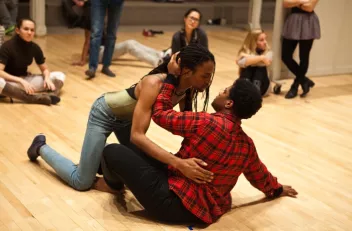 Deux danseurs au sol, sur le point de s'embrasser et des spectateurs autour