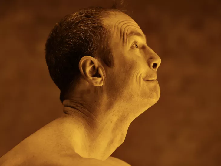 Un homme est de profil, la tête levée vers le ciel, dans une lumière aux tons dorés. Les traits de son visage sont tirés